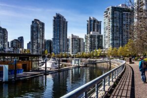 Modern skyscrapers reflect on the serene Vancouver waterfront in a bustling urban scene.