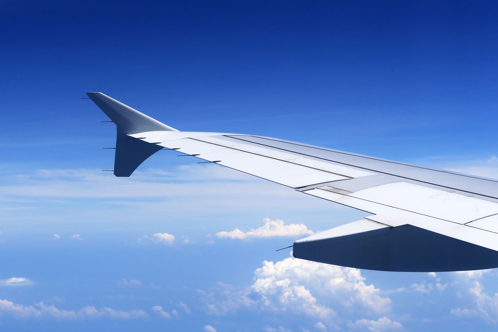 Airplane wing above the clouds against a clear blue sky