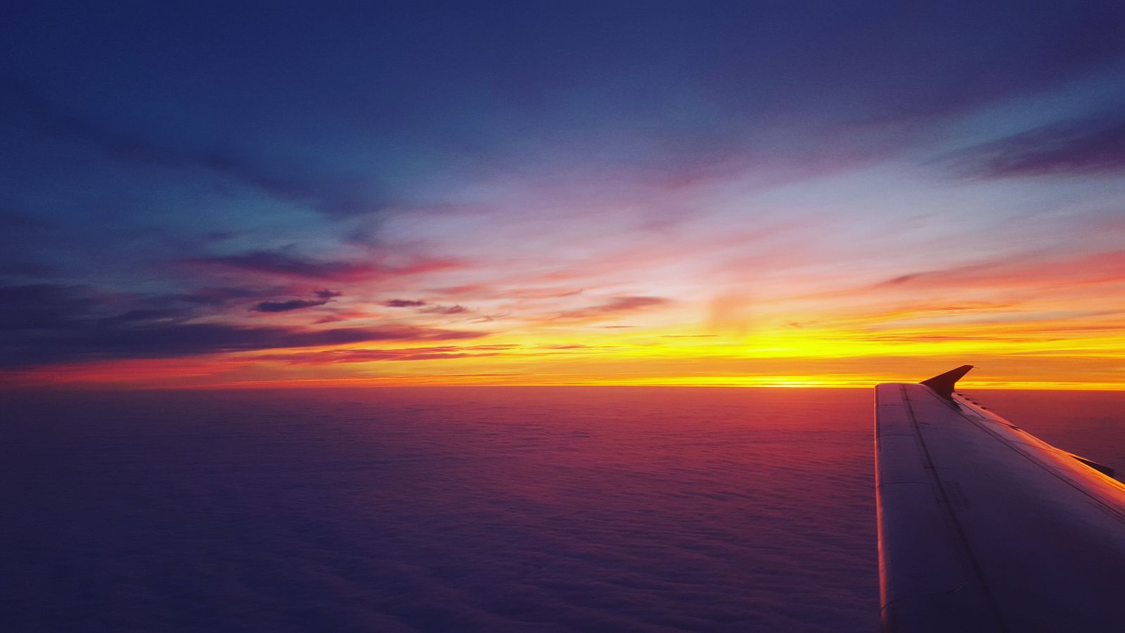 Airplane wing against a sunset sky seen from a window seat