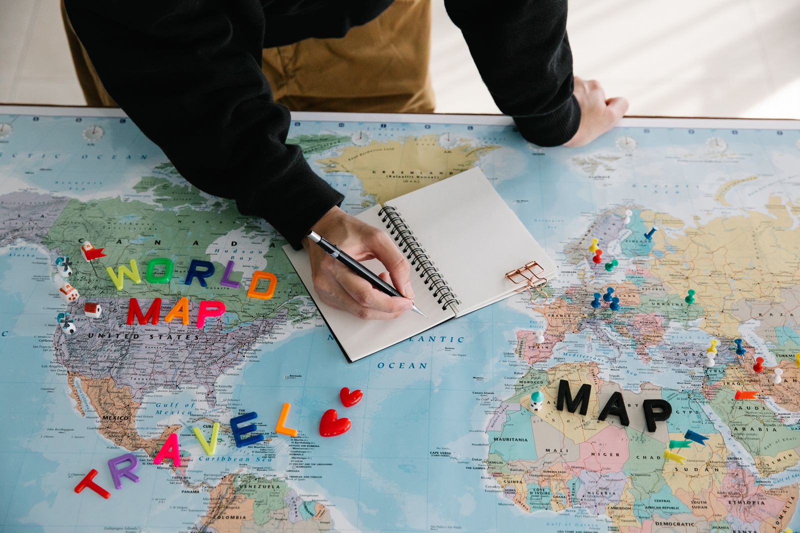 Person writing trip plans in a notebook laid over a world map