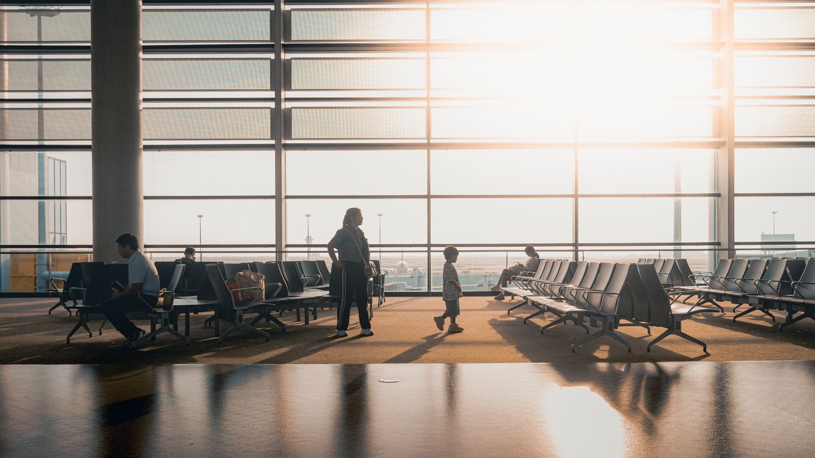 Travellers walking through a bright airport terminal at sunrise with luggage