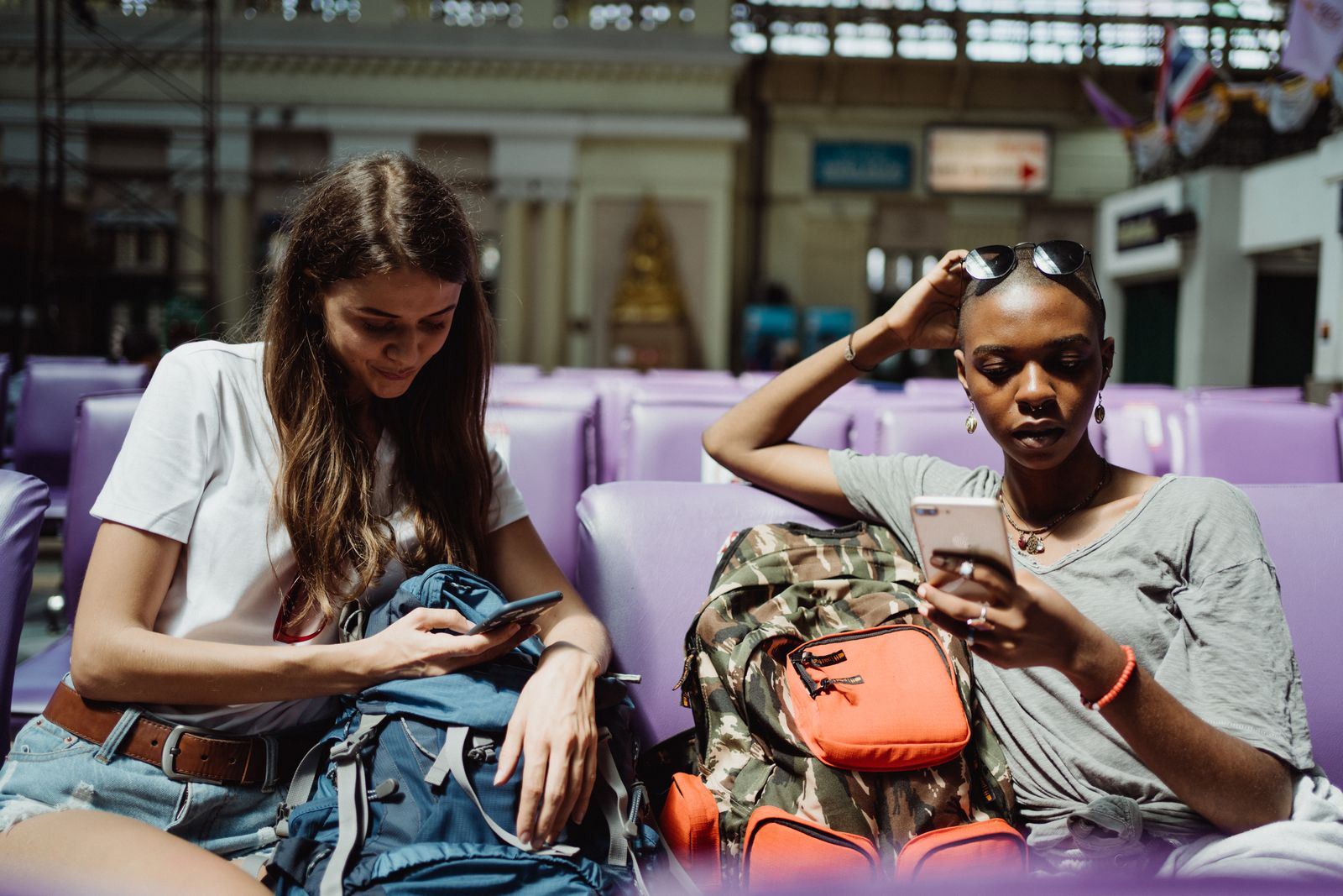 Two travelers checking their trip details on the Stamped travel planner app while waiting at a station