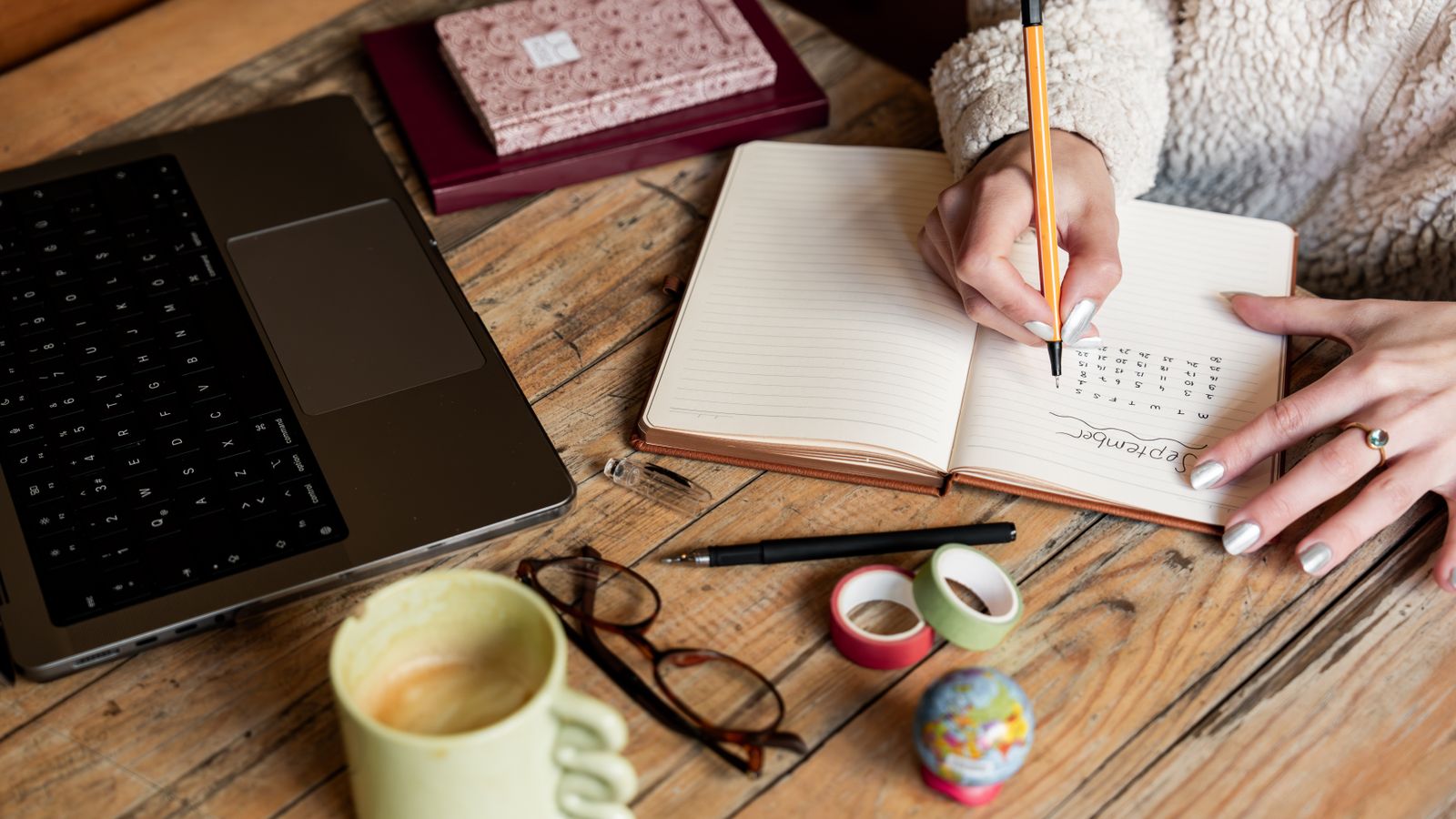 Travel planner writing a day by day custom itinerary in a notepad beside a laptop