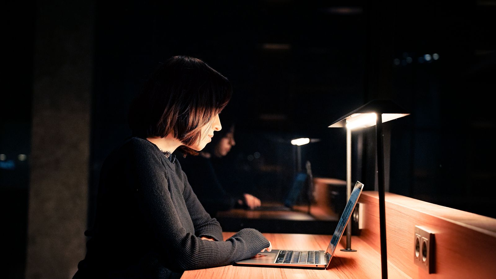 Woman working late at night on a laptop in dim lighting while researching a trip
