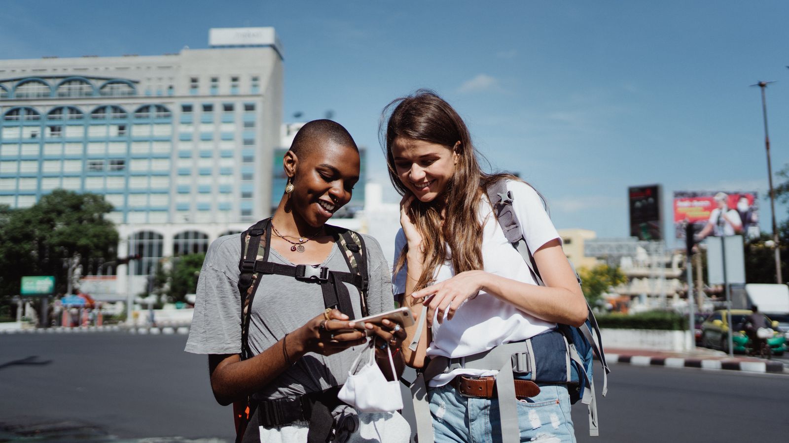 Two travelers standing on a city street looking at a smartphone map trying to navigate
